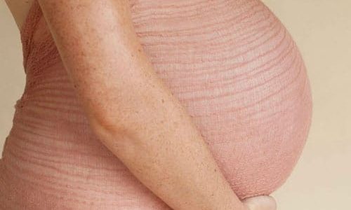 Pregnant woman from the side with her arms cupping the baby